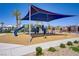 A community playground with swings and slides is covered with a large sun shade and surrounded by small bushes at 2773 Green Envy Ave # 245, North Las Vegas, NV 89086