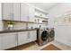 Well-lit laundry room featuring grey cabinets, marble backsplash, open shelves, stainless steel washer and dryer, and tile flooring at 2820 High Range Dr, Las Vegas, NV 89134