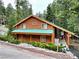 Charming log cabin with a green metal roof and covered porch surrounded by lush greenery and mountain views at 401 Alpine Way, Las Vegas, NV 89124