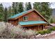 Cozy log cabin with a green roof and stone accents, nestled among tall trees and landscaping at 401 Alpine Way, Las Vegas, NV 89124