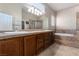 Bathroom with a dual sink vanity, large mirror, and tiled tub with a glass enclosed shower at 5016 Wayfaring Tree Ave, Las Vegas, NV 89131
