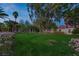 Expansive backyard featuring lush green lawn, mature trees, and colorful flower beds at dusk at 2222 Lucerne Ct, Henderson, NV 89014