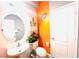 Bright half bath with round mirror, pedestal sink, and orange accent wall at 8156 Blue Hope Diamond Ln, Las Vegas, NV 89139