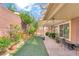 Cozy backyard featuring a covered patio, artificial grass, mature trees, and desert landscaping at 10247 Jamapa Dr, Las Vegas, NV 89178