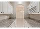 A butler's pantry with granite counters, wine racks, and glass door cabinets, leading to another room with chandelier at 5576 Buena Martina Way, Las Vegas, NV 89141