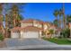 Elegant two-story home featuring a three-car garage, tile roof, manicured lawn, and lush palm trees at 1990 Freeman Ct, Henderson, NV 89014