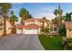 Elegant two-story home featuring a three-car garage, tile roof, manicured lawn, and lush palm trees at 1990 Freeman Ct, Henderson, NV 89014