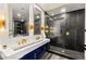 Modern bathroom featuring dual sinks, gold fixtures, a glass shower, and dark tile walls at 2407 Ridgeline Wash St, Las Vegas, NV 89138
