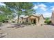 Single-story tan home with desert landscaping, mature trees, a covered patio, and a tile roof at 2323 Barbers Point Pl, Las Vegas, NV 89134