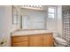 Bright bathroom featuring wood cabinets, a large mirror, granite countertop, and a shower-tub combo with a window at 301 Lakewood Garden Dr, Las Vegas, NV 89148