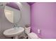 Charming powder room with a round mirror, pedestal sink, and lilac accent wall at 6940 Crescent Gold St, North Las Vegas, NV 89086