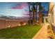 Backyard with green artificial grass, landscaping, and exterior lights at twilight at 7738 Willow Cove Cir, Las Vegas, NV 89129