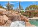 Close-up of rock waterfall and spa, flowing into the pool, accompanied by a shaded tiki hut at 8970 Lansberry Ct, Las Vegas, NV 89147