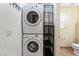 Bright laundry room featuring stacked washer and dryer, shelving for storage, and tile flooring at 9962 Keephills St, Las Vegas, NV 89183