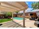 Backyard pool with patio seating underneath a pergola next to lush landscaping and a brick fence at 3717 Shanagolden St, Las Vegas, NV 89129