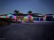 Night shot of a single-story home featuring a three-car garage, palm trees, and holiday lighting at 9865 Bright Angel Way, Las Vegas, NV 89149