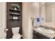 Stylish half bath includes a granite vanity, oval mirror, and floating shelving for storage at 987 Wembly Hills Pl, Henderson, NV 89011