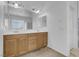 Bathroom with a double vanity, wood cabinets, a large mirror, and bright natural light at 9840 Chief Sky St, Las Vegas, NV 89178