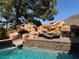 Backyard swimming pool highlighting an adjacent rock waterfall and lounging area for relaxation at 1800 Amarone Way, Henderson, NV 89012