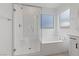 A glass-enclosed shower with seat adjoins a built-in tub in this serene all-white bathroom at 9839 Berkley Brook Ct, Las Vegas, NV 89141