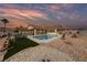This home's outdoor space features a sparkling in-ground pool, desert landscaping, and patio furniture under a colorful sky at 1060 Calico Ridge Dr, Henderson, NV 89011