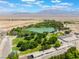 Aerial view highlighting lush greenery, a tranquil pond, and diverse buildings against a backdrop of distant mountains at 8504 Mystic Night Ave, Las Vegas, NV 89143