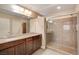 Bathroom featuring a double sink vanity, a glass enclosed shower and a large mirror with bright, modern lighting at 6402 Parrot Ridge Ct, Las Vegas, NV 89139
