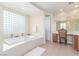 An opulent bathroom with a soaking tub, large window, and vanity with a chair for relaxation at 9992 Peak Lookout St, Las Vegas, NV 89178