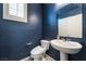Stylish half-bathroom featuring dark blue walls, modern toilet, and a sleek pedestal sink under a window at 7732 Bandon Cliffs St, North Las Vegas, NV 89084