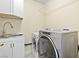 A laundry room features a stainless steel washer and dryer next to a sink with white cabinets for convenient laundry at 8221 Stoneheather Ct, Las Vegas, NV 89117