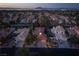 Evening aerial view showcasing a residential community with mature trees, and city lights in the distance at 2108 Inverness Dr, Henderson, NV 89074