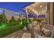 Relaxing backyard with covered patio, string lights, lush artificial turf, brick pavers, and manicured greenery at 10140 Magnolia Creek St, Las Vegas, NV 89141