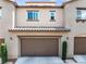 Beige home featuring a two-car garage, brown garage door, tile roof, and concrete driveway flanked by short green shrubbery at 11375 Ogden Mills Dr # 103, Las Vegas, NV 89135