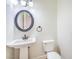 A half bathroom with a pedestal sink, toilet, and round mirror at 5396 Splendido Ave, Pahrump, NV 89061