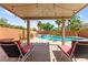 Backyard pool area with sun loungers, palm trees, and a covered patio with lights at 11649 Royal Derwent Dr, Las Vegas, NV 89138