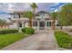 Charming two-story home showcases lush greenery, mature palm trees, and a welcoming circular driveway on a sunny day at 2058 Troon Dr, Henderson, NV 89074