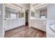 Bathroom with double vanities, decorative mirrors, wood-look floors, and a separate tub and shower at 7606 Kenwood Hills Ct, Las Vegas, NV 89131