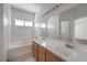 Bright bathroom with dual sinks, large mirror, and bathtub with white tile surround at 7977 Blue Brook Dr, Las Vegas, NV 89147