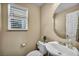Well-lit half bathroom featuring a toilet, sink, mirror and window at 10312 Glimmering Star Dr, Las Vegas, NV 89178