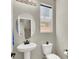 Well-lit powder room with pedestal sink, oval mirror, toilet, and window for natural light at 4533 Queens Hill St, North Las Vegas, NV 89031