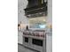 Chef's kitchen featuring stainless steel Wolf range, custom hood, white cabinets, and sleek backsplash at 1404 Reisling Ct, Las Vegas, NV 89144