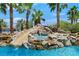 Custom pool featuring a rock waterfall, slide, and surrounding palm trees under a sunny sky at 1404 Reisling Ct, Las Vegas, NV 89144