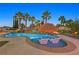 Inviting lagoon style pool with swim up chairs and a thatched umbrella, surrounded by tropical palm trees at 1404 Reisling Ct, Las Vegas, NV 89144