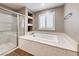Bathroom featuring a soaking tub with marble surround, glass-enclosed shower and a window with plantation shutters at 928 Riverlawn Pl, Las Vegas, NV 89138