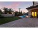 Serene backyard with a sparkling pool, manicured lawn, patio seating, and lush tropical landscaping at twilight at 761 Romano Ln, Henderson, NV 89012