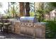 Built-in outdoor kitchen with stainless steel appliances, bar seating, and a view of mature landscaping at 2285 Villefort Ct, Las Vegas, NV 89117