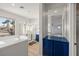 Bright bathroom featuring a soaking tub, walk-in shower with gold trim, and a vanity with a blue cabinet at 323 Harpers Ferry Ave, Las Vegas, NV 89148