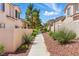 A sidewalk alongside townhomes with a red rock mulch landscape and green plants at 9572 Belle Rich St, Las Vegas, NV 89123