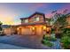 Beautiful two-story home featuring a three car garage, with landscaped front yard and brick driveway at sunset at 326 Caneflower Ct, North Las Vegas, NV 89031