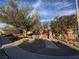 Exterior view of a stone entryway featuring mature trees and landscaping at 5361 Candlespice Way, Las Vegas, NV 89135
